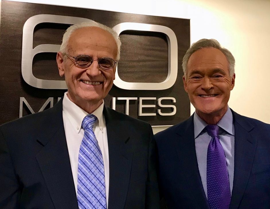 Dr. Duane Priddy Sr. and 60 Minutes correspondent Scott Pelley standing together in front of the 60 Minutes logo