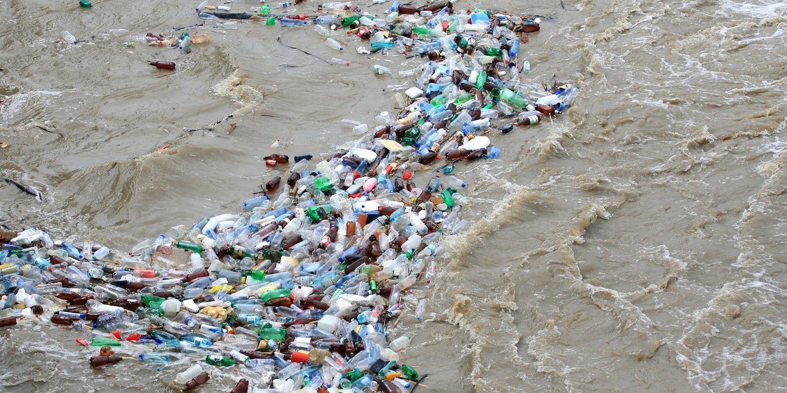 A dense raft of discarded plastic bottles and litter floating on muddy brown river water